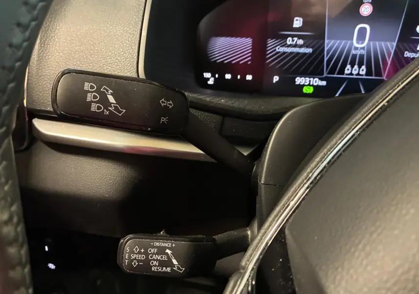 Gros plan sur les commandes au volant d’un Skoda Karoq 2.0 TDI gris, affichage numérique du tableau de bord en arrière-plan.