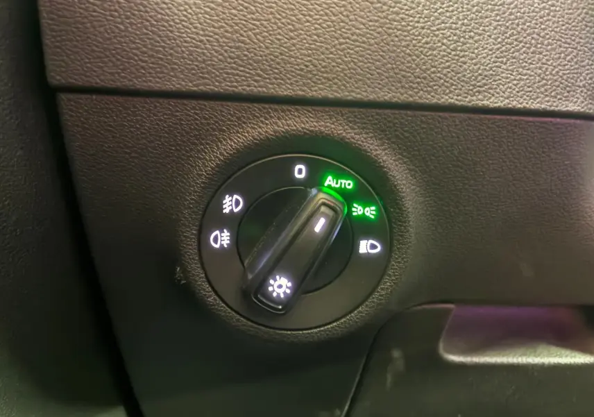 Gros plan sur le bouton de commande des phares du Skoda Karoq 2.0 TDI gris, avec mode automatique activé.