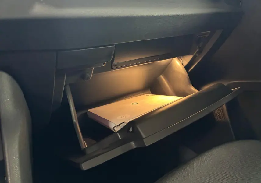 Gros plan intérieur sur la boîte à gants ouverte éclairée du Skoda Karoq gris 2023, avec manuel visible.