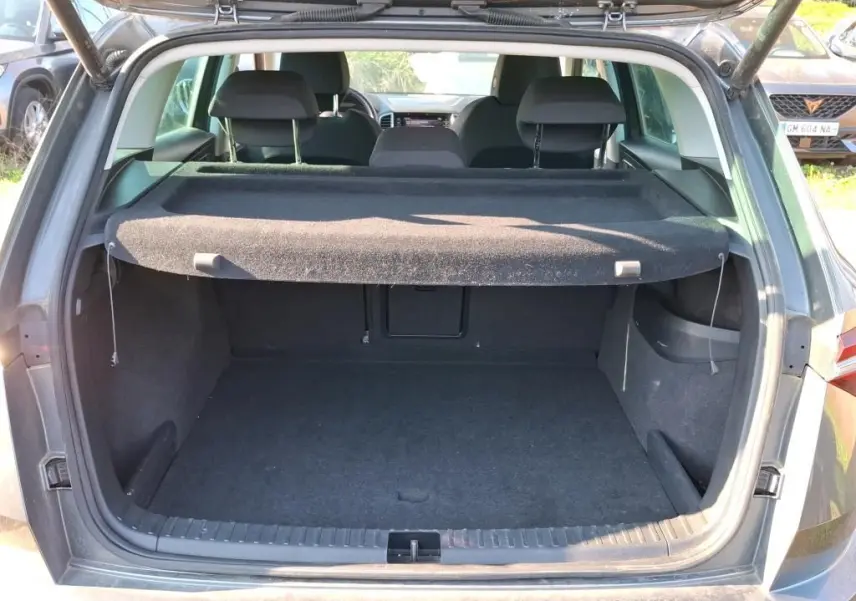 Vue arrière du coffre ouvert d'un SKODA KAROQ gris 2023, montrant l'espace de chargement avec cache-bagages déployé.