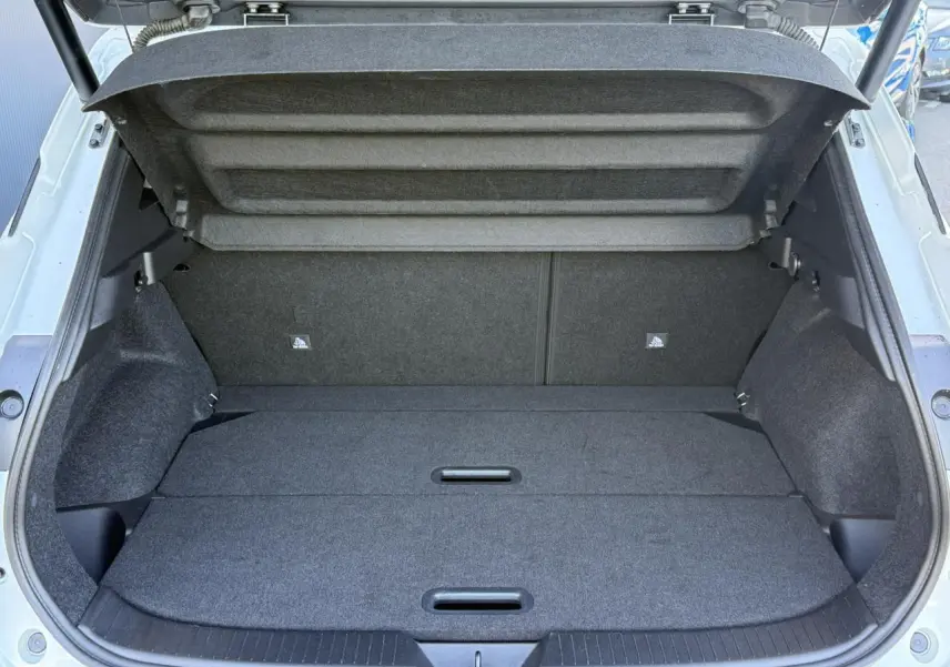 Coffre ouvert vu de l'arrière d'un Nissan Qashqai blanc nacré, espace de chargement plat et tapis gris.