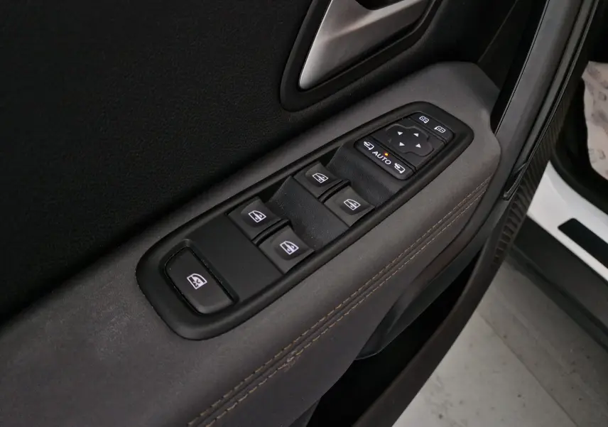 Gros plan sur la commande des vitres électriques côté gauche du Dacia Duster blanc 2024, avec surpiqûres marron visibles.