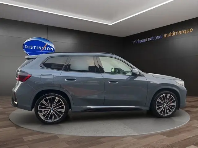 Profil droit d'un BMW X1 Storm Bay 2024 en finition M-Sport avec jantes alliage 20'' et freins rouges, en showroom.