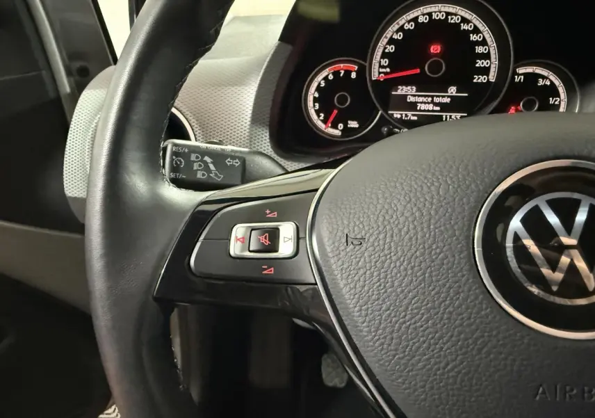 Gros plan sur le volant cuir multifonctions et le tableau de bord éclairé de la Volkswagen Up gris foncé 2022.