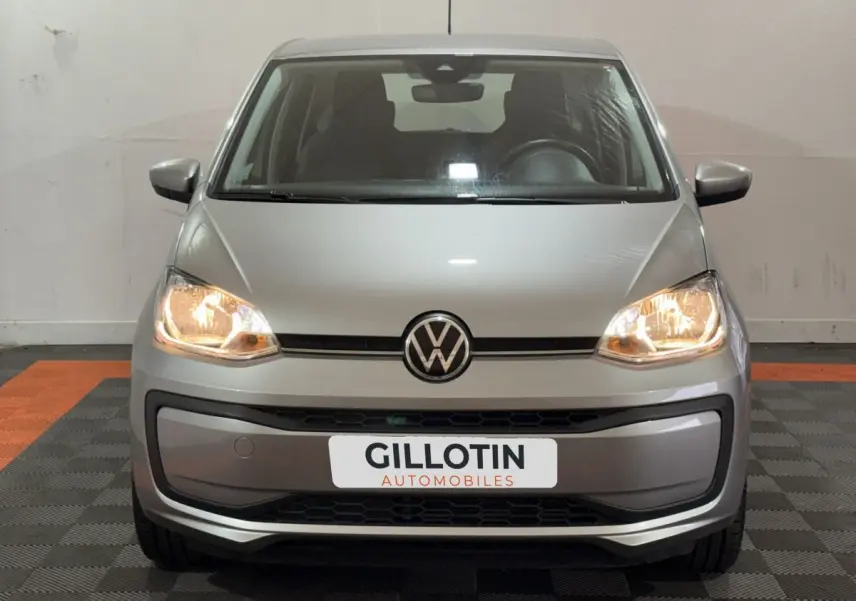 Vue frontale d'une Volkswagen Up gris foncé avec phares allumés et plaque d'immatriculation GILLOTIN AUTOMOBILES.