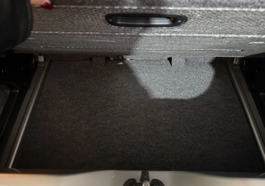 Coffre ouvert du Volkswagen Up gris foncé montrant le compartiment de rangement sous tablette.