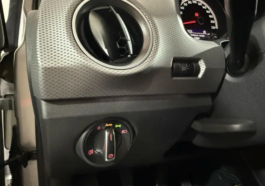 Détail du tableau de bord gris avec commande des phares et aérateur rond dans une Volkswagen Up 2022 vue côté gauche.