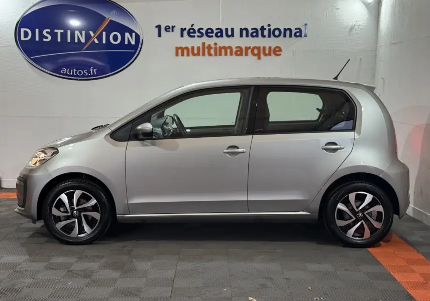 Profil droit d'une Volkswagen Up 1.0 65 Active gris foncé, avec jantes alliage et vitres teintées, en intérieur showroom.