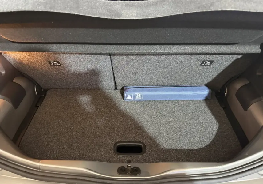 Coffre ouvert de la Volkswagen Up 1.0 65 Active gris foncé, montrant la moquette et un kit de sécurité bleu.