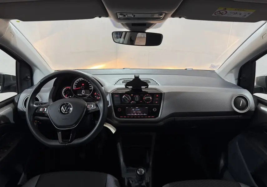 Vue frontale de l'intérieur du Volkswagen Up gris foncé 2022, volant cuir, tableau de bord avec écran et boîte manuelle.