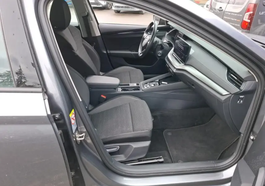 Vue intérieure côté conducteur de la Skoda Octavia Combi gris 2023, montrant sièges tissu et tableau de bord moderne.