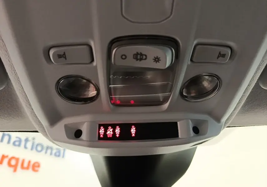 Vue rapprochée du plafonnier intérieur de la Peugeot 208 jaune, avec commandes d'éclairage et voyants de ceinture allumés.