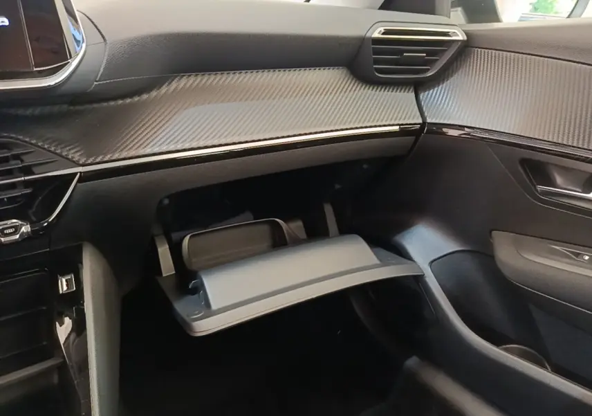 Intérieur de la Peugeot 208 PureTech 75 S&S Active Pack 2023, vue côté passager avec boîte à gants ouverte et tableau de bord noir texturé.