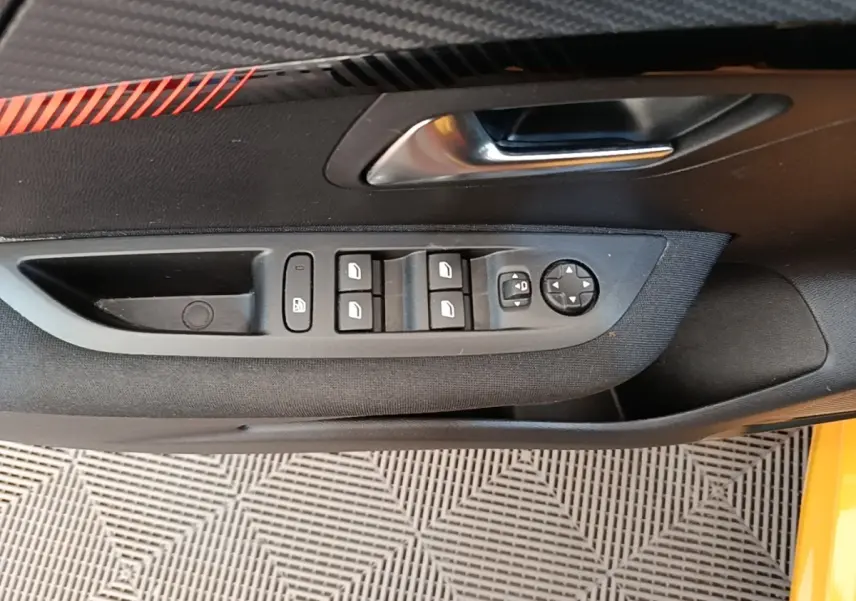 Vue rapprochée de la porte côté conducteur de la Peugeot 208 jaune, montrant les commandes des vitres et rétroviseurs.