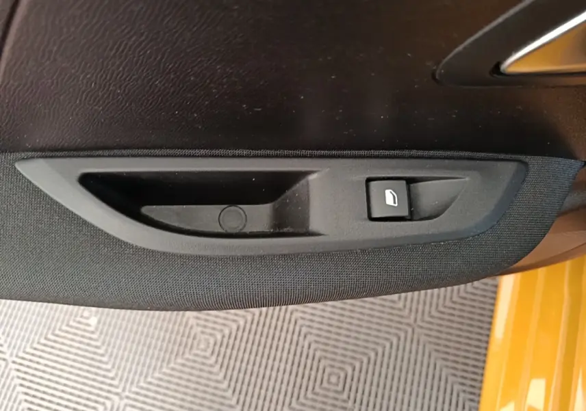 Détail de la commande de lève-vitre côté conducteur sur porte intérieure noire d’une Peugeot 208 jaune.