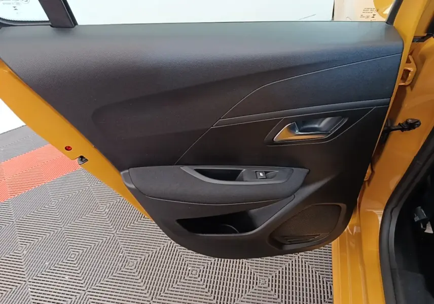 Vue intérieure de la porte avant gauche jaune de la Peugeot 208 2023 avec panneau noir et commande de vitre électrique.