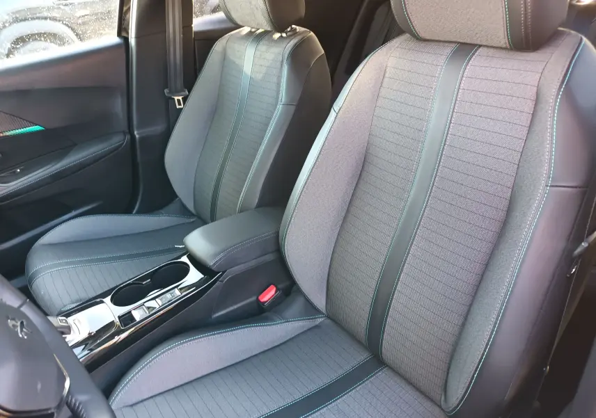 Intérieur avant du Peugeot 2008 noir 2022, sièges en tissu gris avec surpiqûres bleues et console centrale brillante.