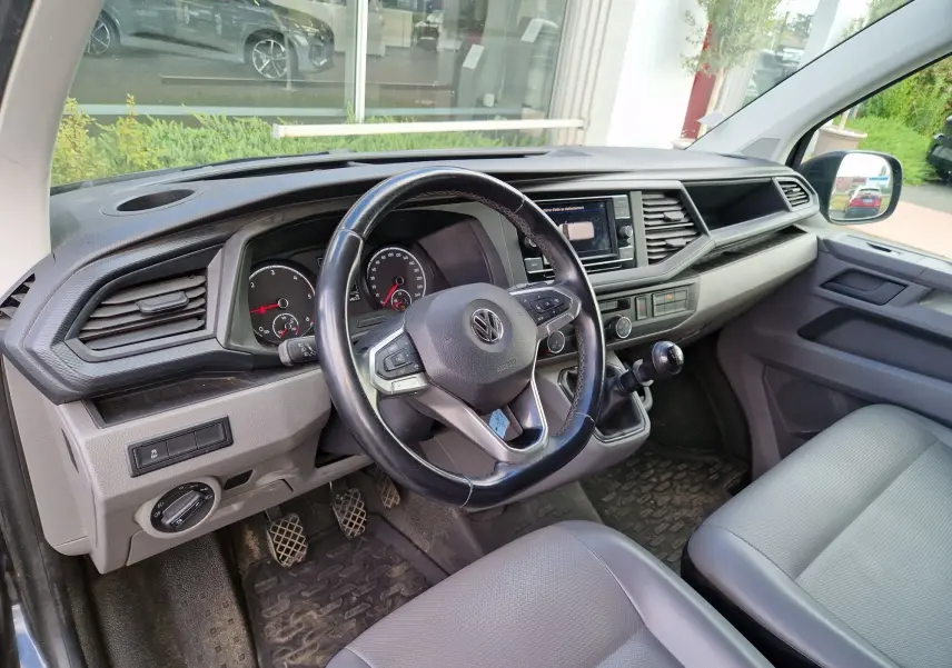 Vue intérieure côté conducteur du Volkswagen Transporter noir 2020, volant multifonction et tableau de bord moderne visibles.