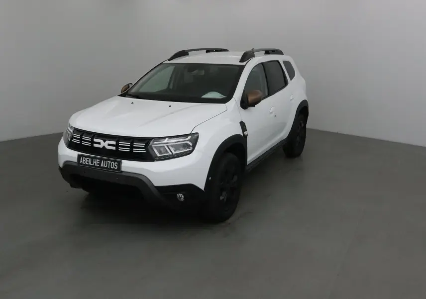 Dacia Duster blanc 2024 en 3/4 avant droit avec rétroviseurs bronze et jantes noires dans un studio gris.