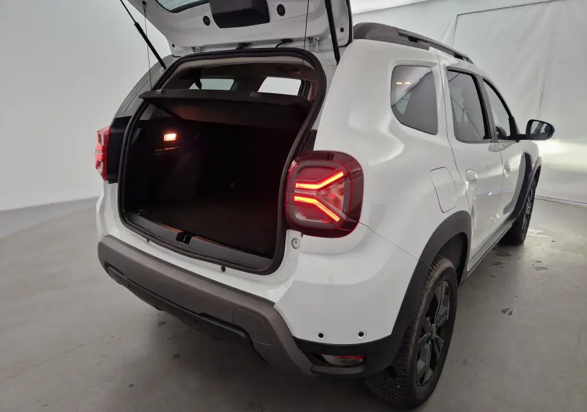 Vue arrière droite d'un Dacia Duster blanc 2024 avec coffre ouvert et feux arrière allumés dans un studio.