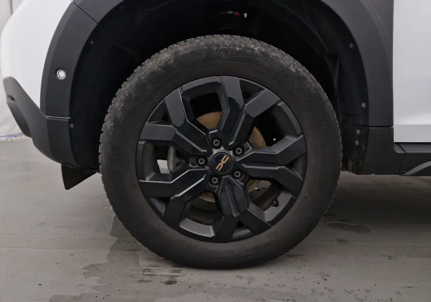 Gros plan sur la roue avant gauche noire avec jante spécifique du Dacia Duster 4x4 blanc 2024.
