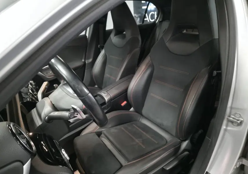 Intérieur côté conducteur d'une Mercedes Classe A gris, sièges sport noirs avec surpiqûres rouges visibles.