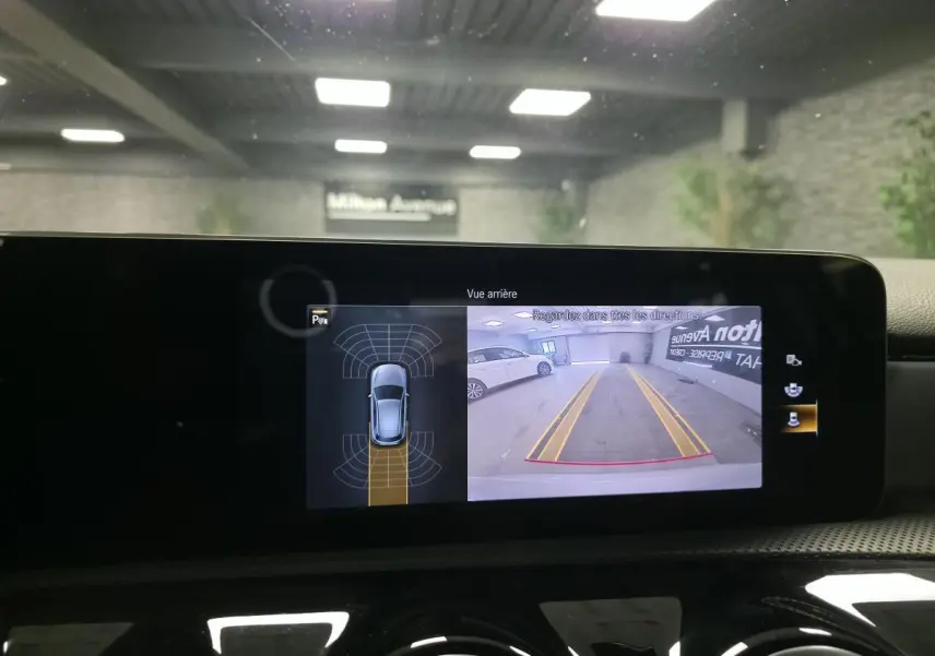 Affichage de la caméra de recul sur l'écran central d'une Mercedes Classe A gris, vue arrière avec lignes de guidage jaunes.