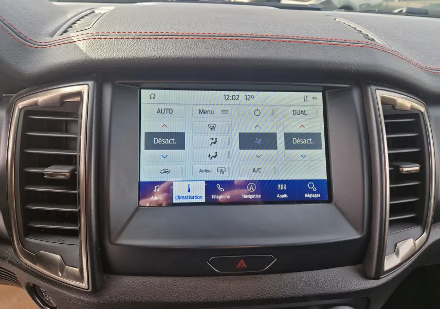 Écran tactile central du Ford Ranger Raptor 2022 montrant les commandes de climatisation, entouré de sorties d'air et surpiqûres rouges.