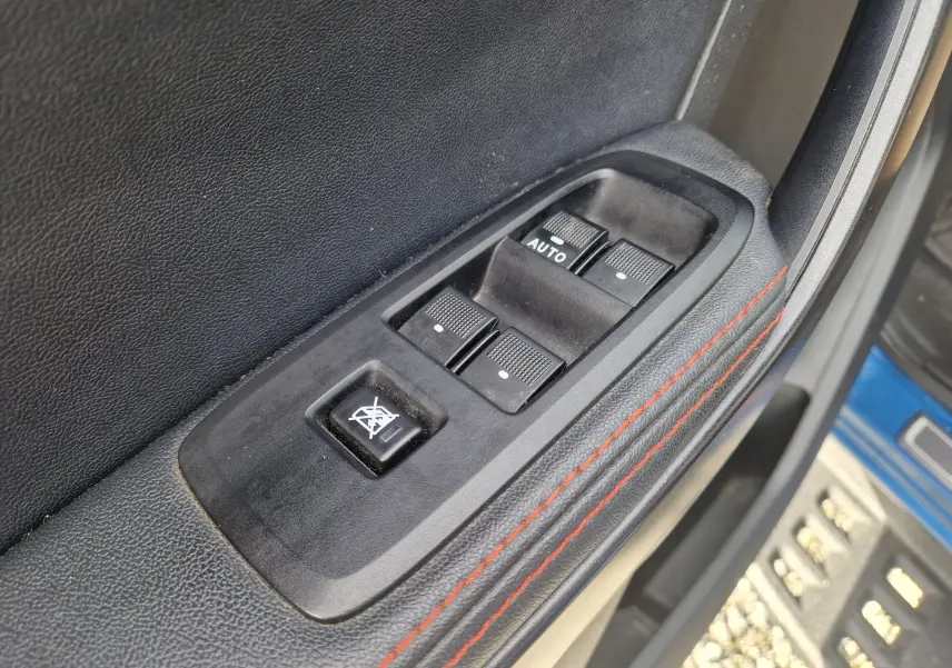 Gros plan sur les commandes des vitres électriques côté conducteur du Ford Ranger Raptor 2022 avec surpiqûres rouges.