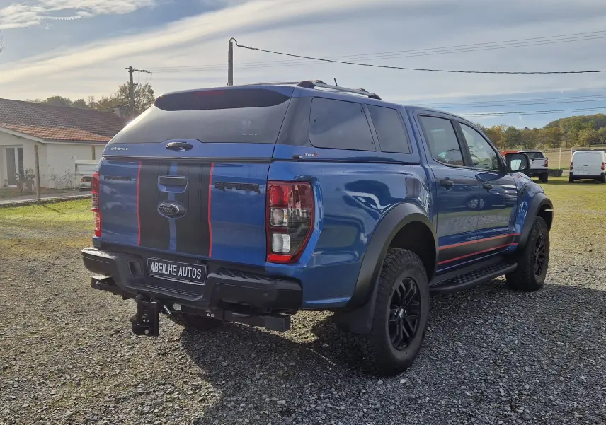 Vue 3/4 arrière droite du Ford Ranger Raptor bleu Ford Performance avec hard top et bandes noires et rouges sur la benne.