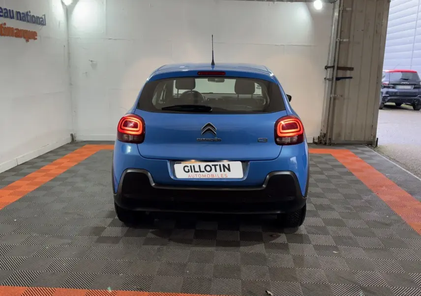 Vue arrière d'une Citroën C3 bleu vif avec feux arrière allumés dans un garage éclairé.