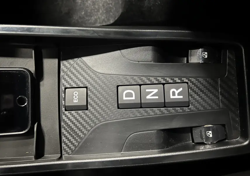 Gros plan sur la console centrale noire à effet carbone de la Ligier JS50 BEV 8KWH ELITE avec boutons de boîte auto et commandes vitres.