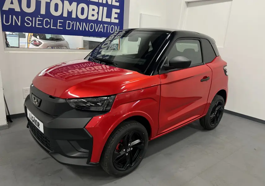 Vue 3/4 avant d'une LIGIER JS50 BEV 8KWH ELITE rouge avec toit noir et jantes alu noires en intérieur showroom.