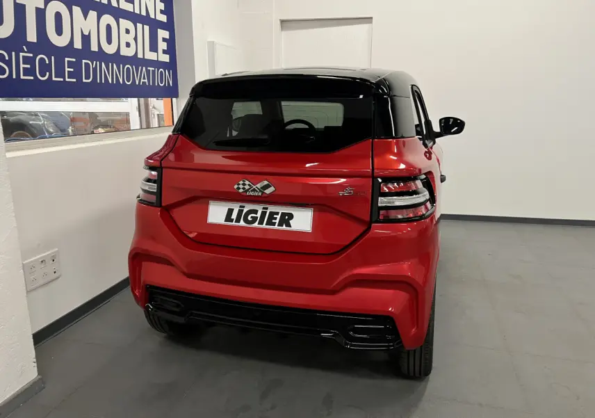 Vue arrière d'une Ligier JS50 BEV 8KWH ELITE rouge avec toit noir et feux arrière LED dans un showroom.