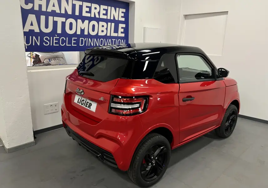 Vue 3/4 arrière droite de la LIGIER JS50 BEV 8KWH ELITE rouge avec toit noir et jantes alu noires en intérieur showroom.