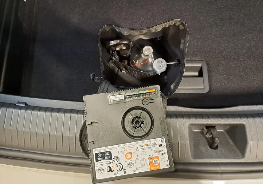 Vue plongeante sur le coffre d'un Volkswagen Tiguan argent Dolomite, montrant un kit de réparation pneu et compresseur.