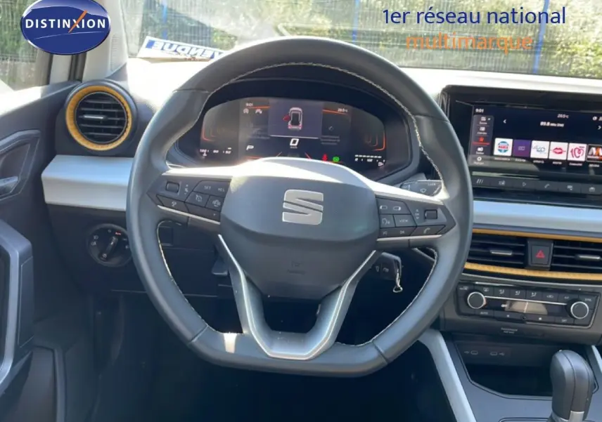 Vue intérieure centrée sur le volant multifonction d'une SEAT Arona 2025, tableau de bord digital et écran tactile visibles.
