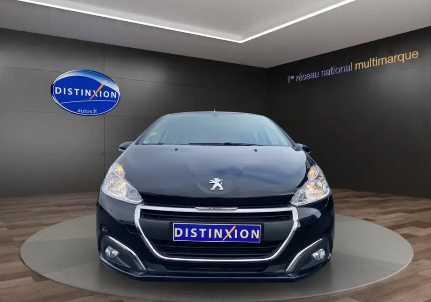 Peugeot 208 AFFAIRE noir vue de face, avec calandre chromée et phares allumés dans un showroom.