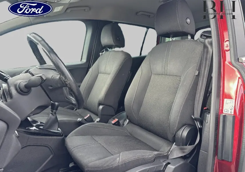 Vue intérieure côté conducteur du Ford B-MAX rouge Premium Candy, montrant les sièges avant en tissu gris et le volant cuir.