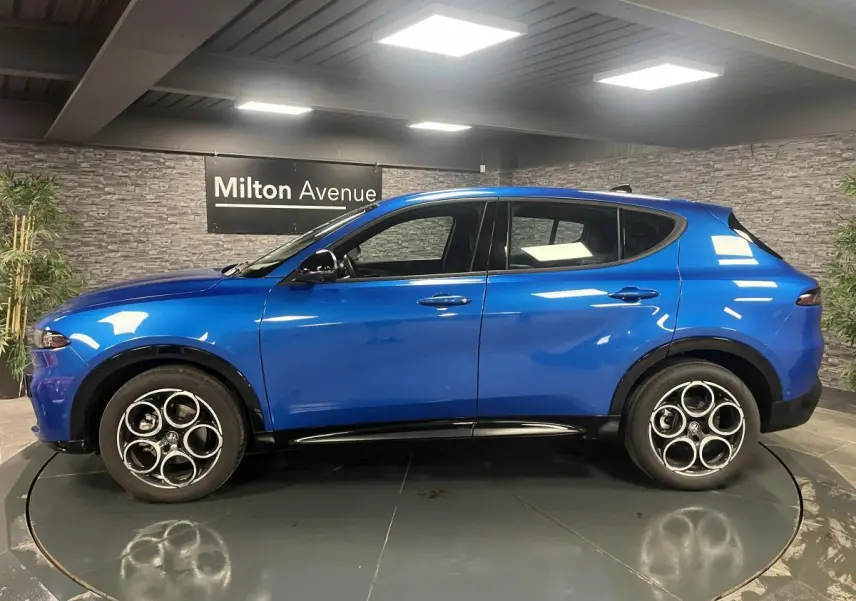 Profil côté gauche de l'Alfa Romeo Tonale Sprint 2024 bleu métallisé avec jantes alliage 18 pouces en intérieur showroom.