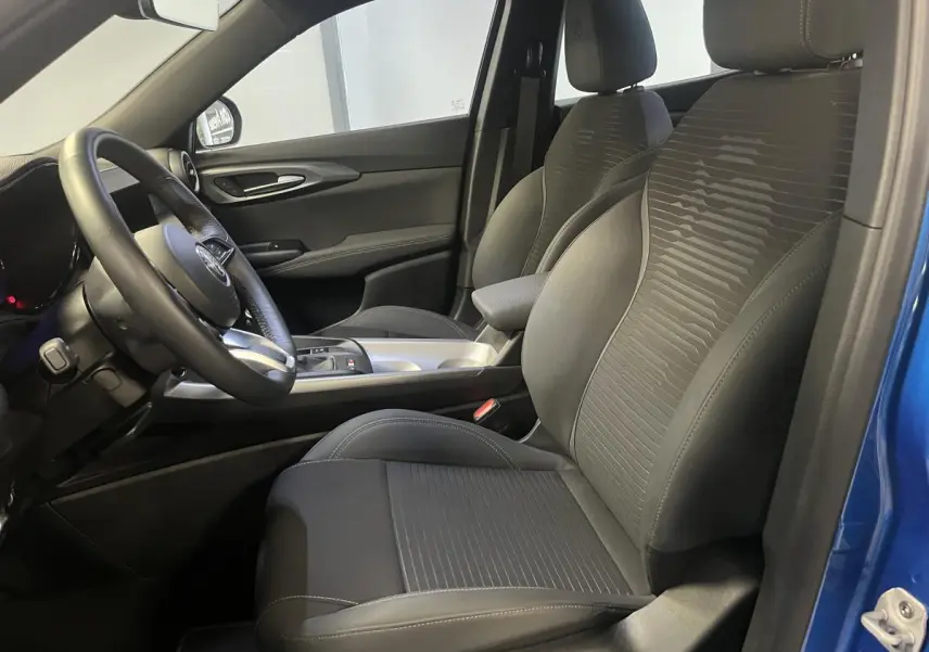 Vue intérieure côté conducteur de l'Alfa Romeo Tonale bleu, avec sièges tissu noir et volant sport cuir.