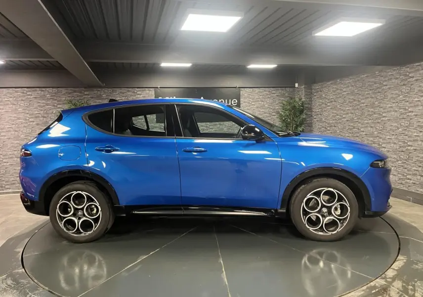 Profil côté gauche d'un Alfa Romeo Tonale Sprint 2024 bleu métallisé avec jantes noires en intérieur showroom.