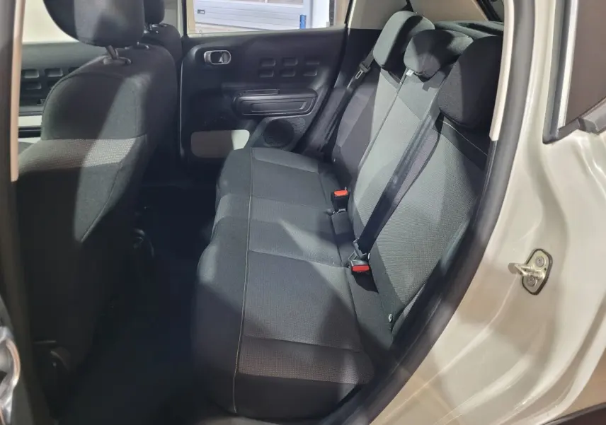 Vue intérieure côté droit sur la banquette arrière noire d'une Citroën C3 beige 2022 avec appuie-têtes et ceintures.