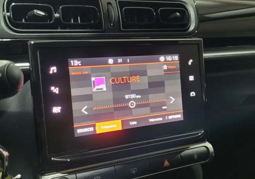 Écran tactile central allumé montrant radio FM dans l'habitacle noir d'une Citroën C3 beige de 2022.