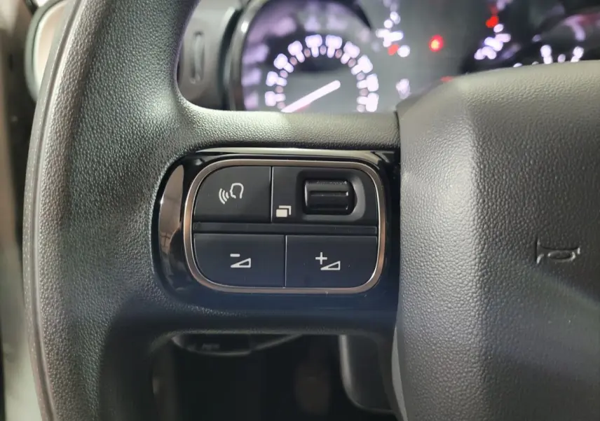 Gros plan sur les commandes du volant côté gauche de la Citroën C3 beige PureTech 2022 avec tableau de bord flou en arrière-plan.