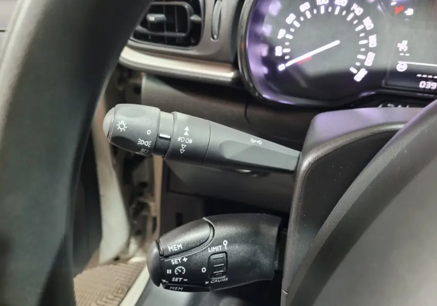 Gros plan sur le volant et les commandes de régulateur de vitesse d'une Citroën C3 beige, tableau de bord partiellement visible.