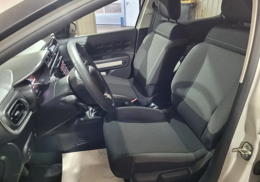 Vue intérieure côté conducteur de la Citroën C3 beige 2022, montrant sièges noirs et tableau de bord avec écran tactile.