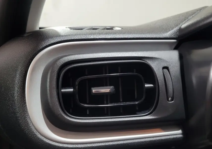 Gros plan sur la sortie d'air rectangulaire noire avec contour argenté du tableau de bord d'une Citroën C3 beige.