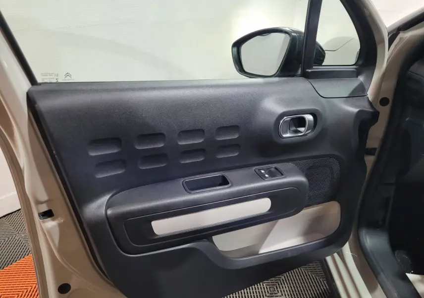 Vue rapprochée de la porte avant gauche beige de la Citroën C3 avec son panneau intérieur noir et beige et commandes électriques.