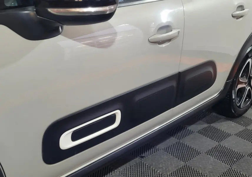 Gros plan sur la porte côté gauche beige d'une Citroën C3 2022 avec protection noire distinctive et rétroviseur noir.